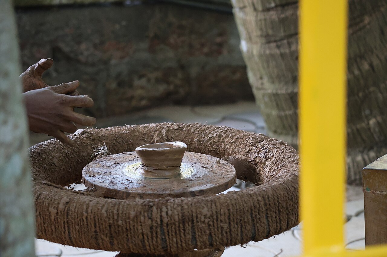 A potter's hands shaping clay on the wheel — an age-old echo of God forming man from the dust of the ground (Genesis 2:7).