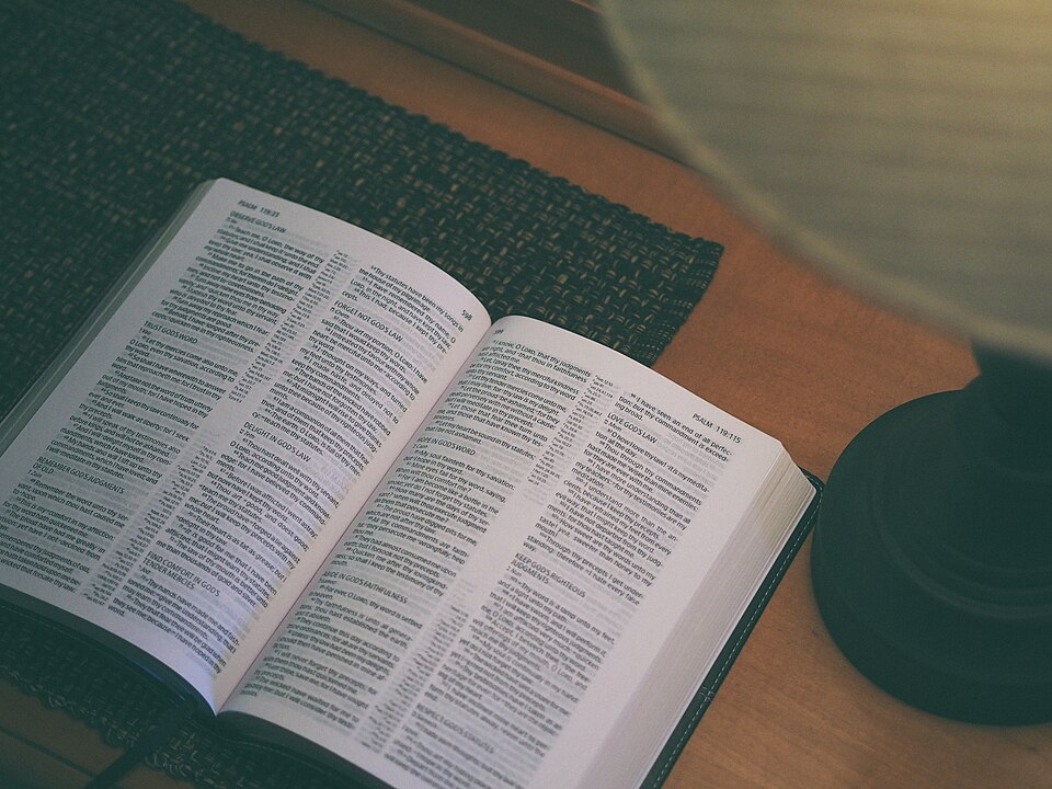 A Bible open to Psalm 119 under a desk lamp