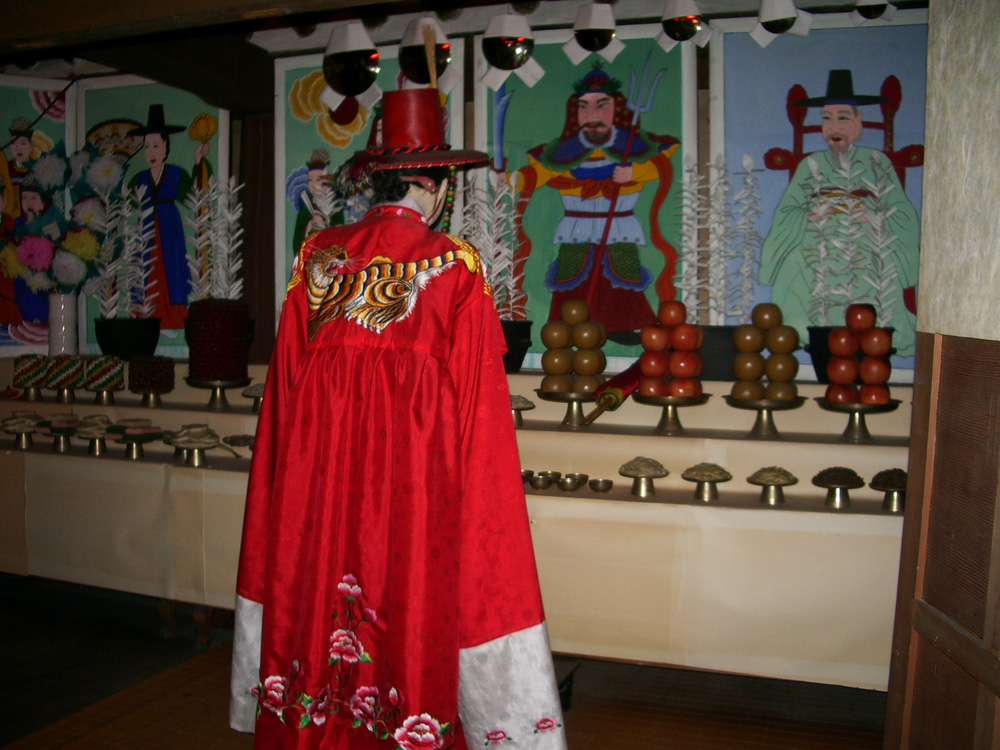A diorama recreating a Korean shaman ritual (gut) at the Lotte World Folk Museum — a shaman seen from behind before an altar