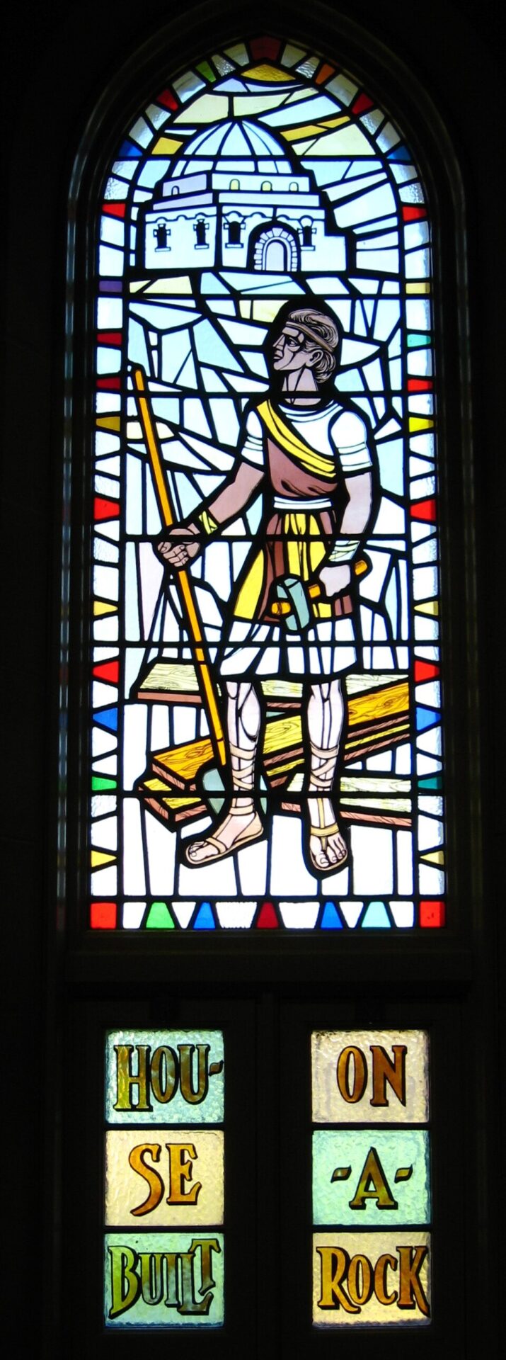 A house built on the rock (stained-glass window) — whoever hears the word and 'does' it is the wise builder on the rock (Matthew 7:24-25).