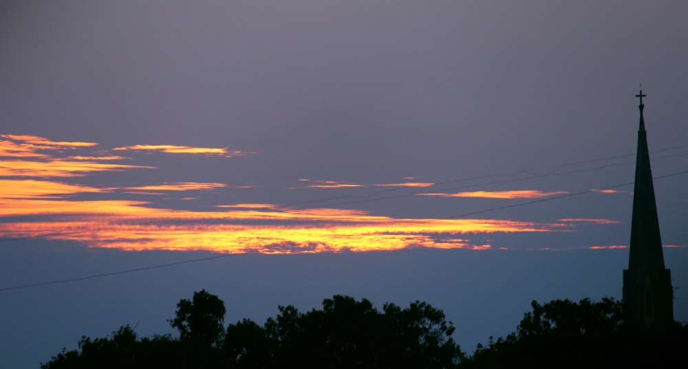 The silhouette of a church steeple cross against an evening sky