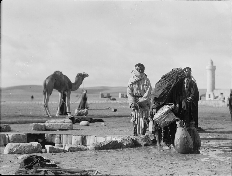 An early 20th-century black-and-white photograph of the ancient well at Beersheba, with camels and people drawing water