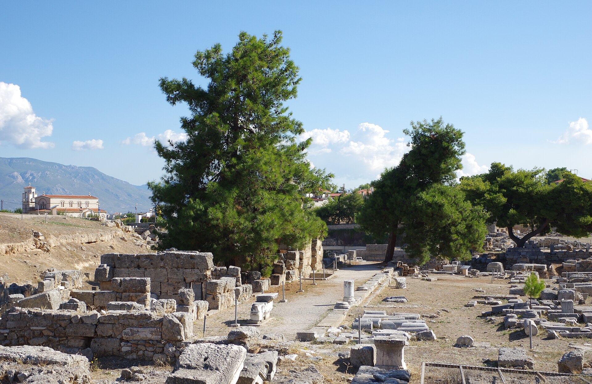Ruins of the ancient agora at Corinth, Greece, with fallen stone foundations and pine trees