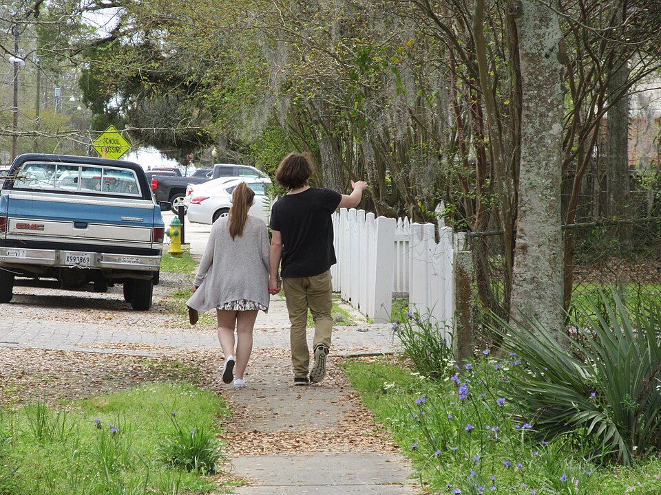 Two people seen from behind walking beside a white fence