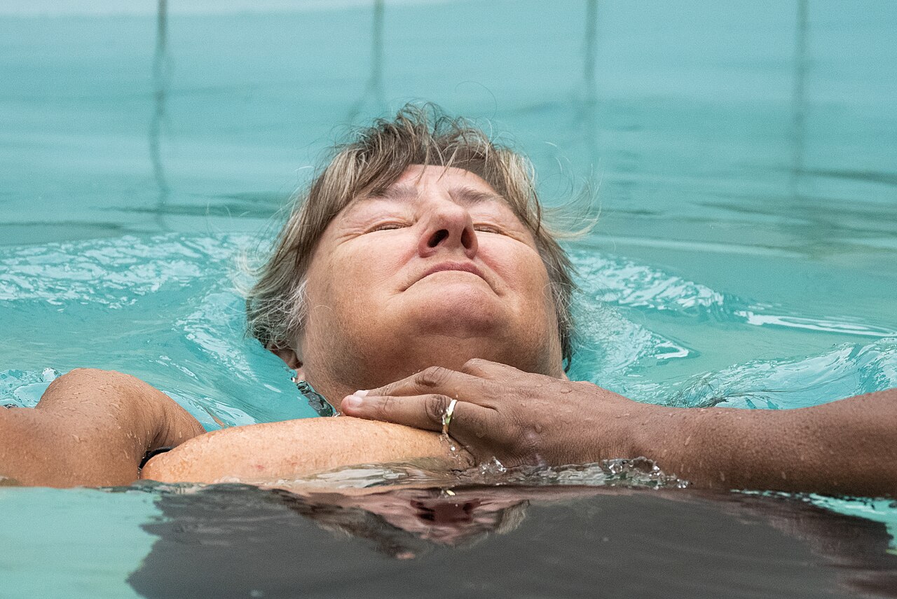 A baptism participant reclining in the water with support from the officiant