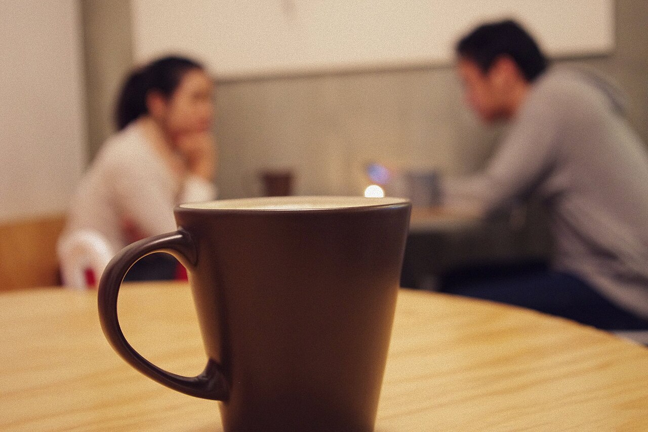 Two people sit facing each other in conversation at a café, a reminder to listen to others in everyday encounters.