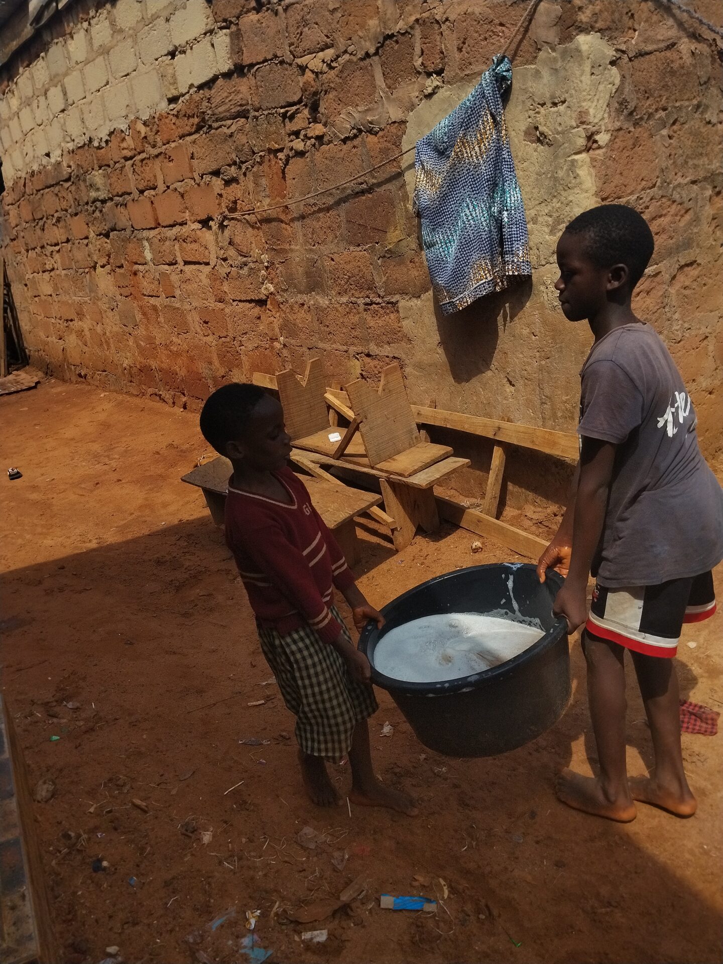 Two children holding opposite sides of a black basin of water