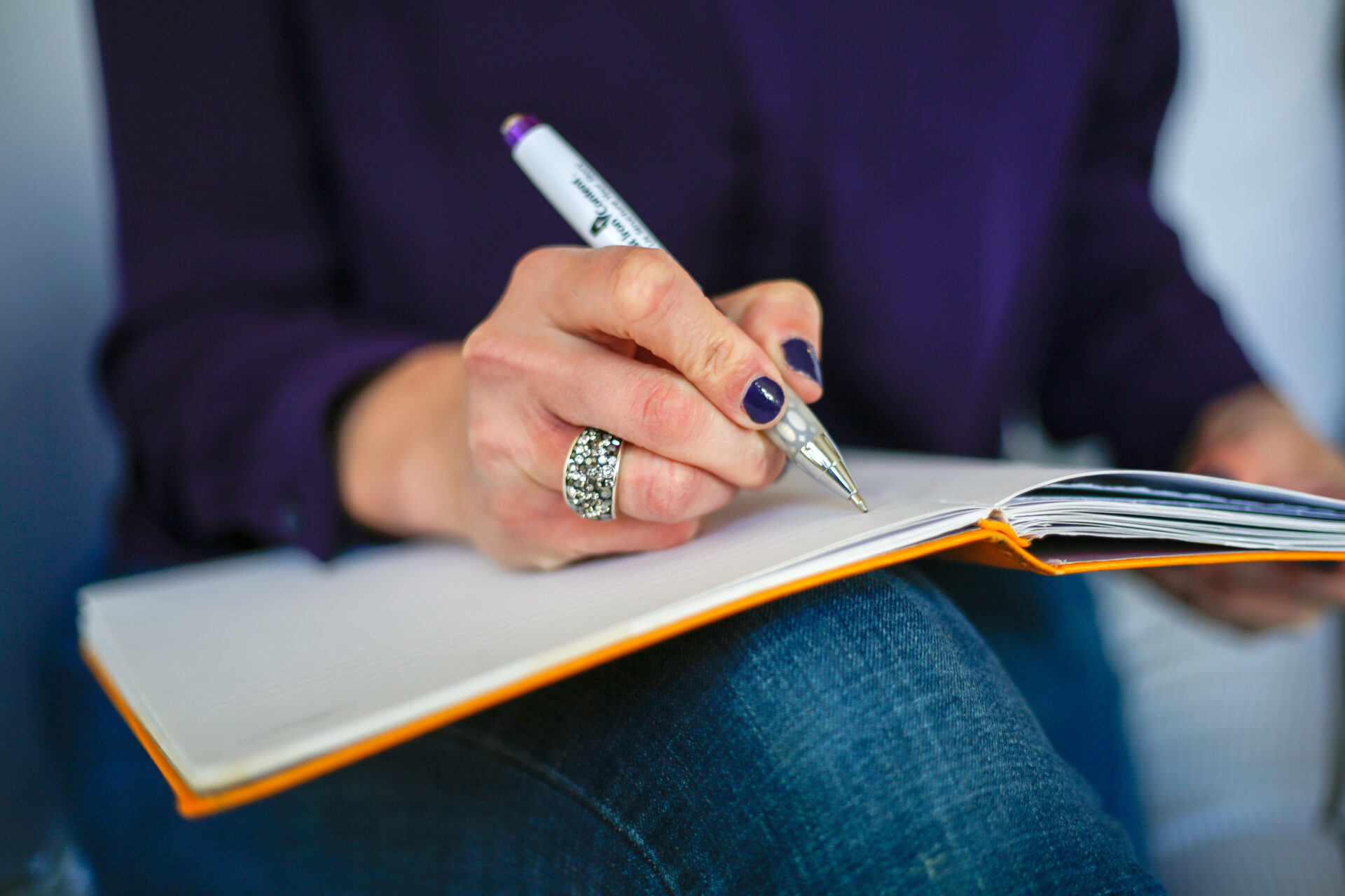 A hand writing with a pen in an open notebook on a lap