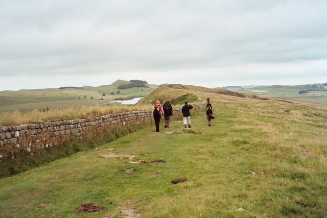 People walking together on a grassy path beside a low stone wall